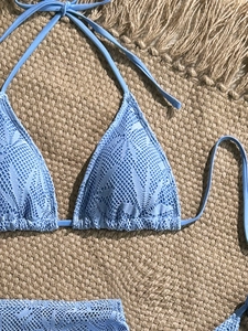 Dettaglio di un bikini all'uncinetto azzurro con motivo a foglie su un tappeto da mare