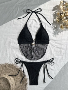 Dettaglio bikini nero con anello dorato e inserto in rete su sfondo di tessuto bianco
