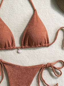 Detail of terracotta smocked bikini with seashell pendant on a beach holiday background