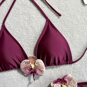 Detail of burgundy bikini top featuring pleated cups and a decorative orchid accessory
