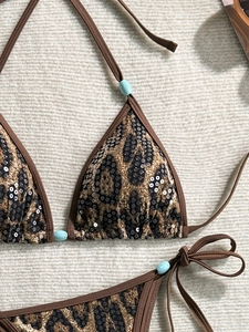 Detail of leopard print bikini with sequins and turquoise bead accents on white fabric