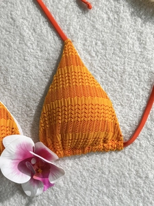 Detail of bright orange bikini top with textured wave knit fabric on white background