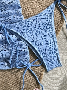 Dettaglio del bikini in pizzo azzurro con motivo floreale a rete su stuoia di paglia