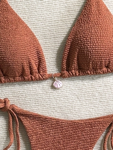 Detail of rust red textured bikini top with a delicate pink shell charm and ribbed fabric
