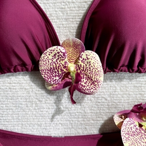 Detail of magenta bikini top with ruched triangle cups and purple orchid floral decoration