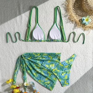 Flat lay of a three-piece floral bikini set including a matching green sarong and top