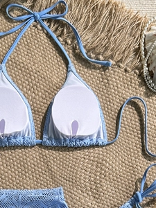Posa piatta del bikini in pizzo azzurro con allacciatura al collo su stuoia di paglia