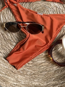 Burnt orange bikini bottoms on straw mat with beach accessories for summer