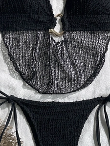 Dettaglio del top bikini nero con fibbia dorata e tessuto a bolle strutturato su bianco