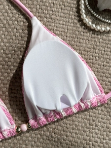 Pink and white knit bikini top with removable pads and beaded details on straw background
