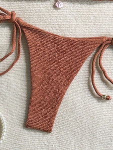Close-up of rust red bikini bottom with shell charm and textured fabric detail