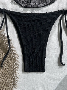 Dettaglio slip bikini nero all'uncinetto con laccetti laterali e trama in maglia traforata