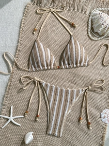 Detail of knit striped bikini with beads, shells and starfish on beige woven mat