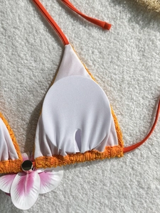 Detailed macro view of orange lace bikini top with white lining and faux flower embellishment