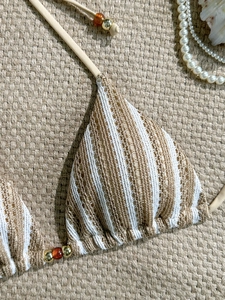 Detail of crochet striped bikini top with amber and gold bead drawstring on a straw mat