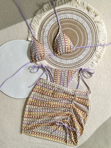 Flat lay of a crochet three-piece bikini set with striped skirt on a boho rug