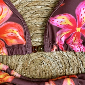 Detail view of tropical floral print bikini top with decorative beads on beach straw mat