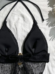 Dettaglio del top bikini nero con bordo in pizzo a rete e anello metallico dorato