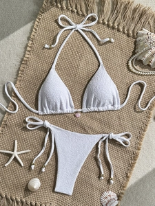 Flat lay of white textured bikini set with a pink shell charm and beach decorations