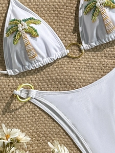 Bikini blanc deux pièces avec broderie palmier et anneaux dorés sur fond de paille tressée