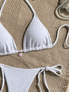 Detail of white textured bikini with pink shell pendant on a beach-themed woven mat