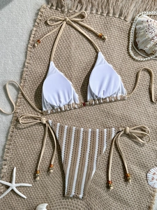 Flat lay of textured crochet striped bikini with decorative amber beads on straw mat