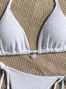 Close-up of white seersucker bikini with pink scallop pendant on woven straw background