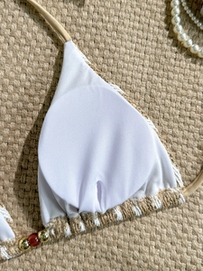 Detail of white crochet bikini top with hanging beads and knit border on straw mat
