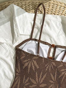 Maillot de bain crochet marron avec motif ajouré et perle ambre sur un tapis de paille