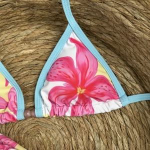 Detail of floral bikini top with tropical print and beaded center on straw background