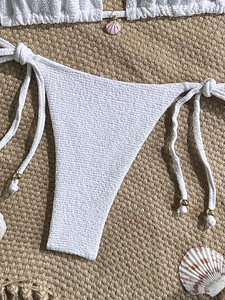 Detail of white waffle texture bikini with side ties, pink shell charm, and gold beads