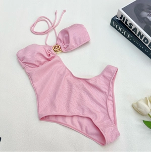 Pink textured halter swimsuit with gold buckle and cutout detail on a styled background