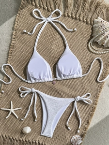 Detail of white textured bikini with shell pendant and gold beads on jute mat