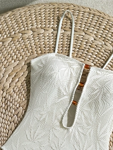 Détail du tissu en dentelle blanche du maillot avec perles ambre et texture de feuilles