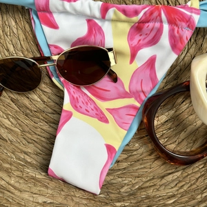 Detailed view of floral bikini bottoms with blue side ties on a beach hat background