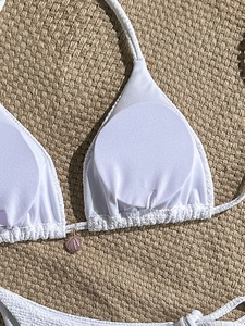 Close-up of white smocked bikini top featuring a decorative pink shell pendant detail