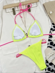 Detailed flat lay of a fluorescent yellow bikini with pink ties on a vacation background