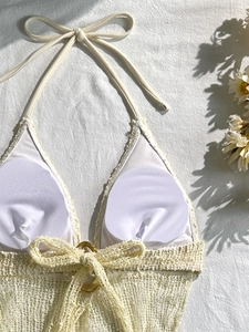 Dettaglio del top bikini all'uncinetto crema con anello dorato e trama in maglia elegante
