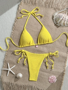 Detailed flat lay of a textured yellow bikini with pink shell charm and sea decor