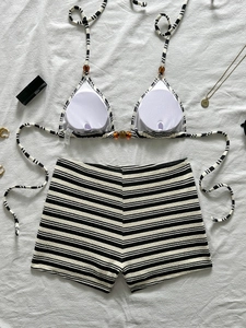 Bikini a righe bianche e nere con top allacciato al collo e pantaloncini a vita alta su bianco
