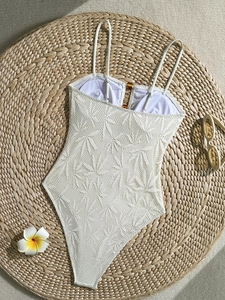 Texture détaillée du maillot de bain en dentelle blanche avec motifs tropicaux et anneaux