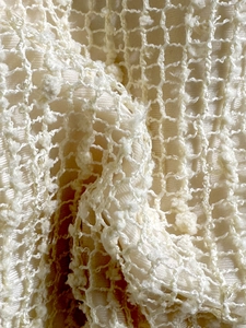 Vista macro del tessuto bikini crema con pizzo a rete e dettagli pompon testurizzati 3D