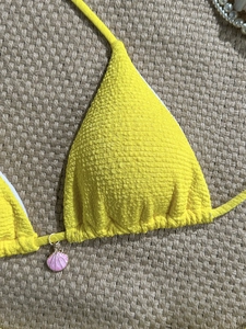 Detail of yellow textured bikini top with pink shell pendant on beach mat