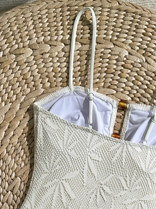 Détail de maillot de bain en dentelle blanche avec motifs et boutons ambrés sur fond paille