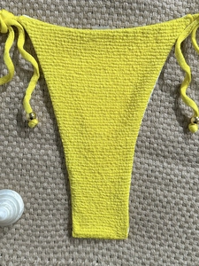 Detail of yellow crinkle bikini bottom with side ties and gold beads on beach mat