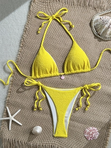 Flat lay of yellow crinkle fabric bikini with shell charm and starfish beach props