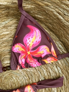 Floral halter bikini top with lily print and beaded detail on woven straw background