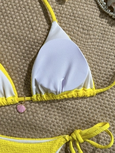 Close-up of yellow seersucker bikini fabric with pink shell charm on woven mat
