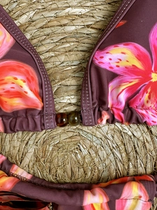 Floral print bikini top with amber bead detail on a natural woven mat background