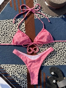 Flat lay of pink bikini set with floral texture on beach mat with vacation accessories